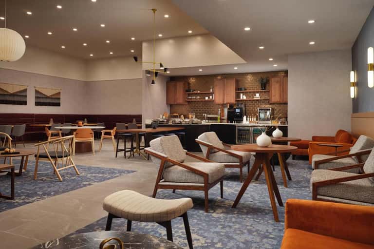 Modern hotel common area with seating, kitchen, bar, wood accents, and mid-century inspired furnishings