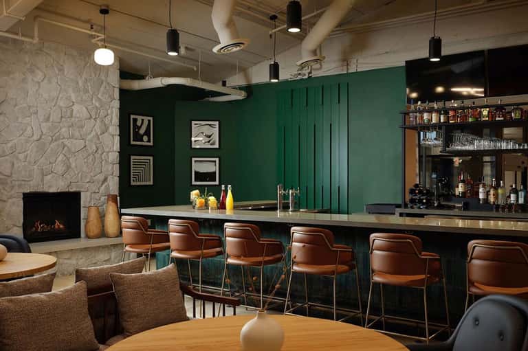 Modern hotel bar with green walls, fireplace, leather seating, and illuminated bar counter