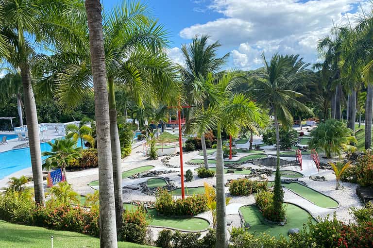 Miniature golf course surrounded by palm trees, pools, and lush tropical landscaping
