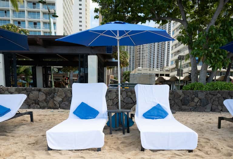 Two lounge chairs with blue pillows and umbrella on sandy beach area