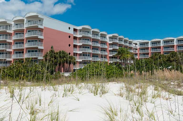 Red and white beachfront residential building with multiple balconies and sandy dunes below