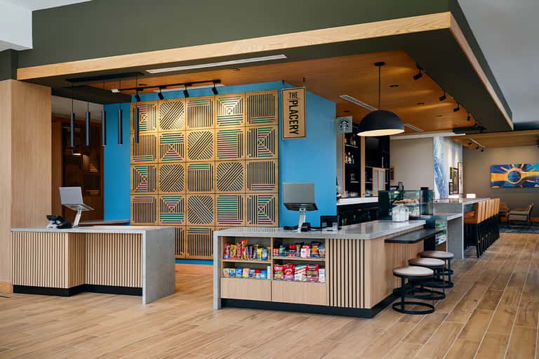 Contemporary hotel café with blue accent wall, wooden geometric feature wall, counter service, and modern seating
