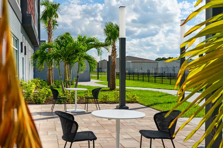 Outdoor seating area with black chairs, white tables, palm trees, and yellow architectural elements