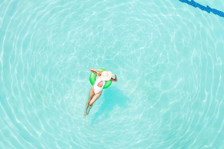 Aerial view of woman floating on green inflatable in crystal-clear turquoise pool