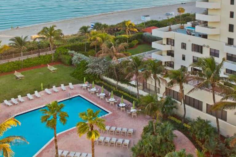 Aerial view of resort pool, lawn, and white apartment buildings overlooking beach