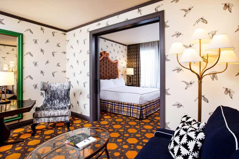 Eclectic hotel room with bird wallpaper, orange patterned carpet, green doorframe, and vintage-inspired furnishings