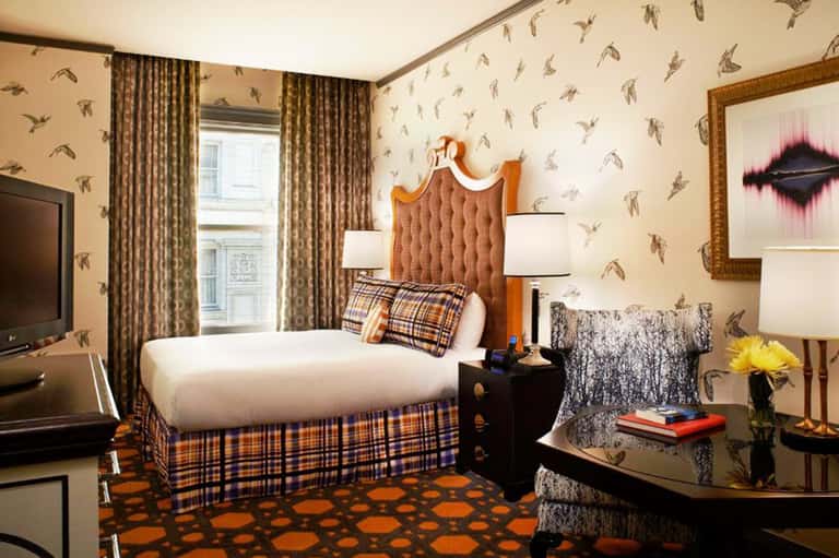 Boutique hotel bedroom with bird-patterned wallpaper, plaid details, and city window view