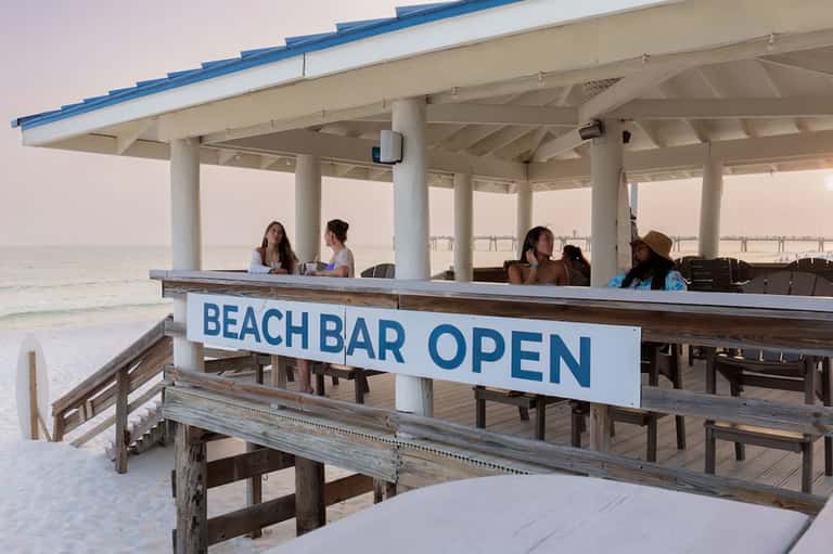 Beachfront bar pavilion with white columns and patrons enjoying ocean views