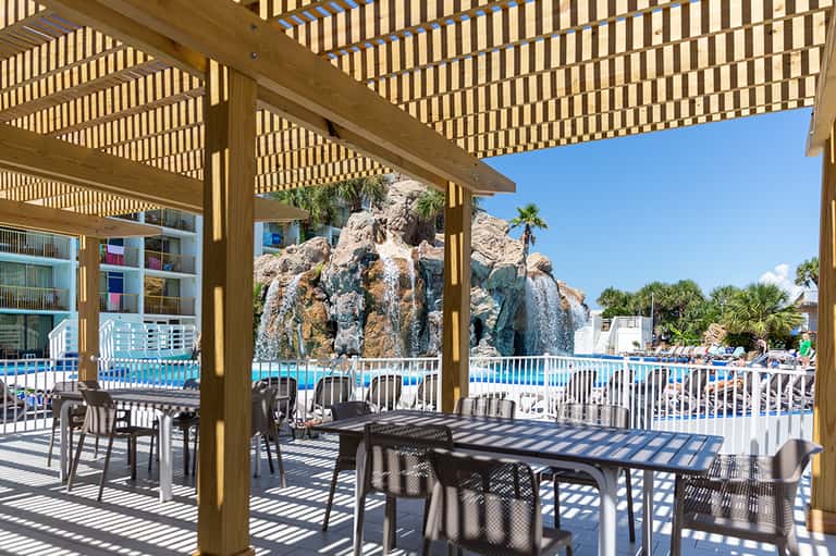 Shaded resort patio with wooden pergola, dining tables, and rocky landscape feature