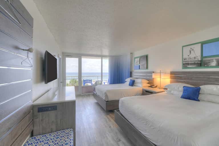 Beachfront hotel room with twin beds, ocean view balcony, flat-screen TV, and blue accents