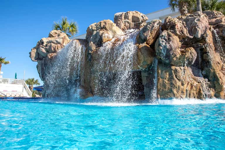 Rock waterfall feature in resort pool with cascading water and clear turquoise water below