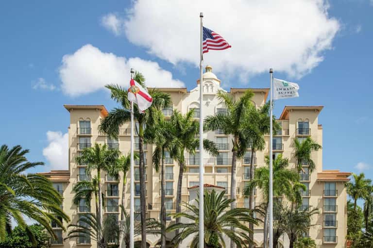 Historic hotel building with cream facade, palm trees, and flags flying in daylight