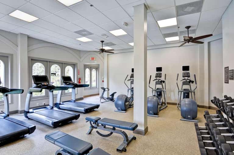 Bright fitness center with treadmills, ellipticals, and dumbbells near glass doors