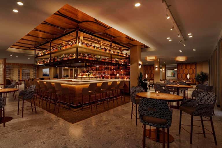 Upscale bar lounge with wooden ceiling panels, elevated bar, ambient lighting, and seating
