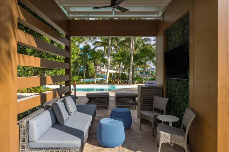 Covered outdoor lounge with seating overlooking the resort pool and tropical landscape