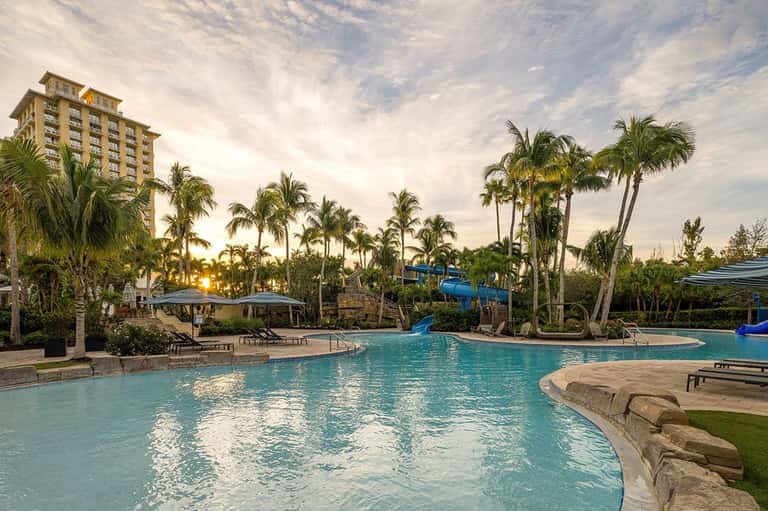 Sprawling resort pool complex with palm trees, cabanas, and multi-level turquoise swimming areas