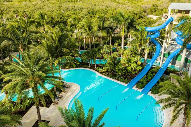 Aerial view of tropical resort pools surrounded by palm trees with blue water slides