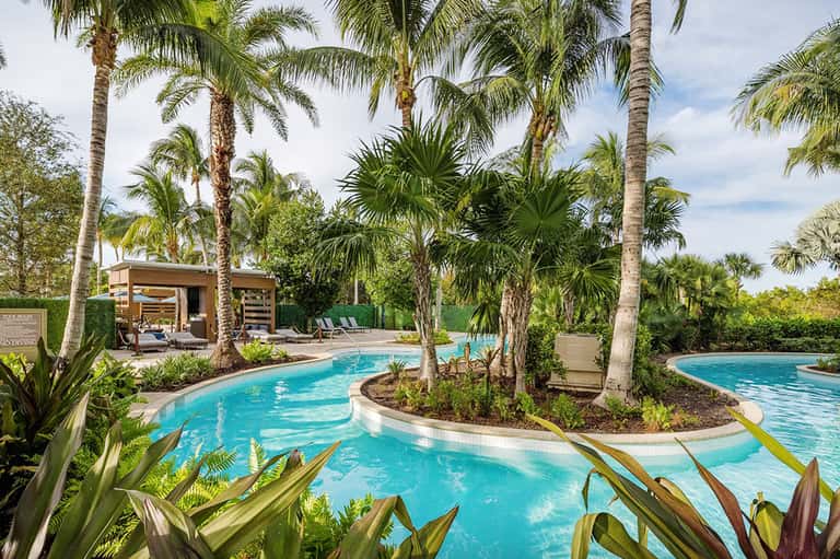 Lagoon-style resort pool with turquoise water, palm trees, tropical plants, and cabana pavilion
