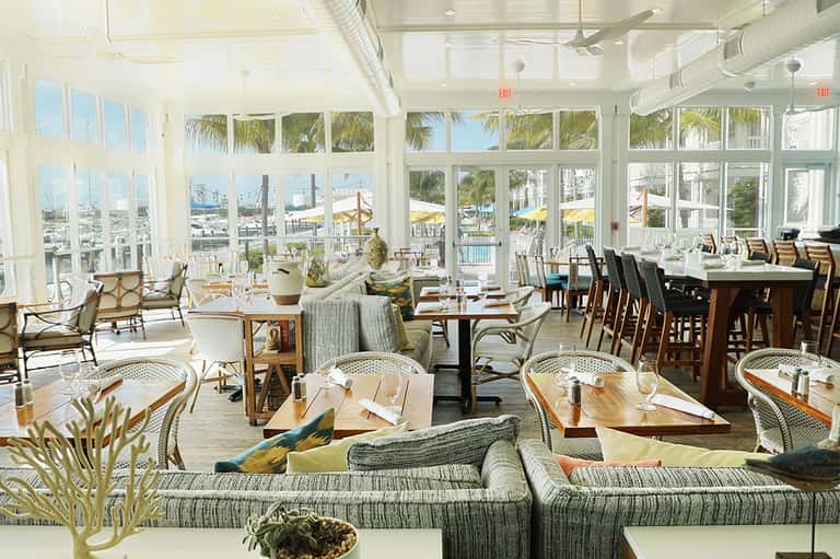 Bright beachfront dining room with floor-to-ceiling windows overlooking pool and beach areas