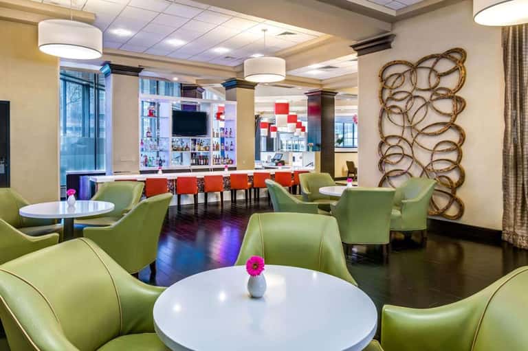 Modern hotel lounge with green chairs, bar area, and contemporary decor