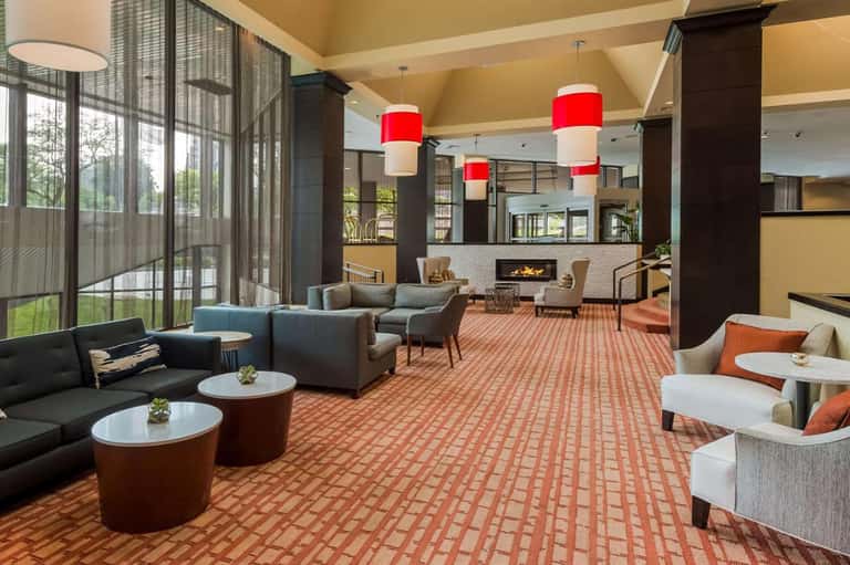 Spacious hotel common area with fireplace, red pendant lights, and modern seating arrangements