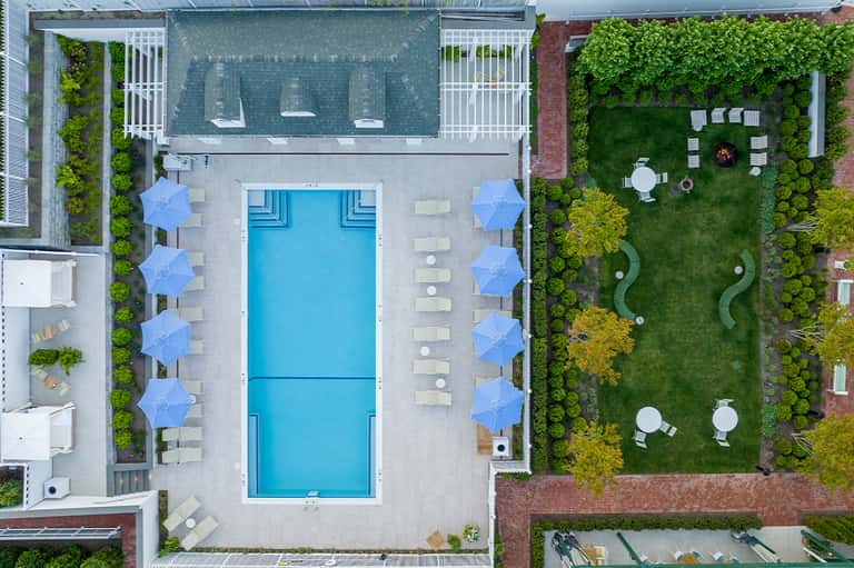 Aerial view of resort pool deck with blue umbrellas, lounge chairs, manicured lawns, and landscaped gardens