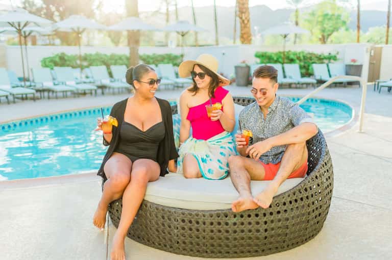 Three people sitting on woven lounge chair by resort pool with tropical mountains in background