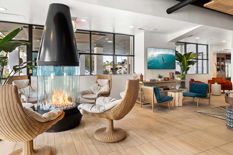 Luxury resort lobby with suspended fireplace, woven chairs, ocean view, and modern design