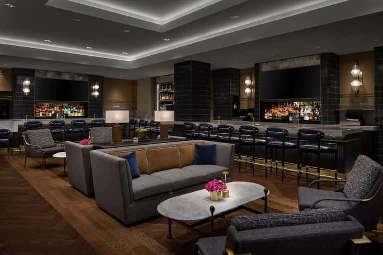Luxury hotel media room with recliners, bar, multiple screens, and sophisticated decor