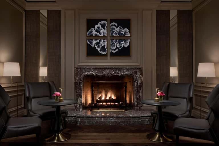 Luxury lounge with fireplace, black leather chairs, ornate marble surround, and modern art