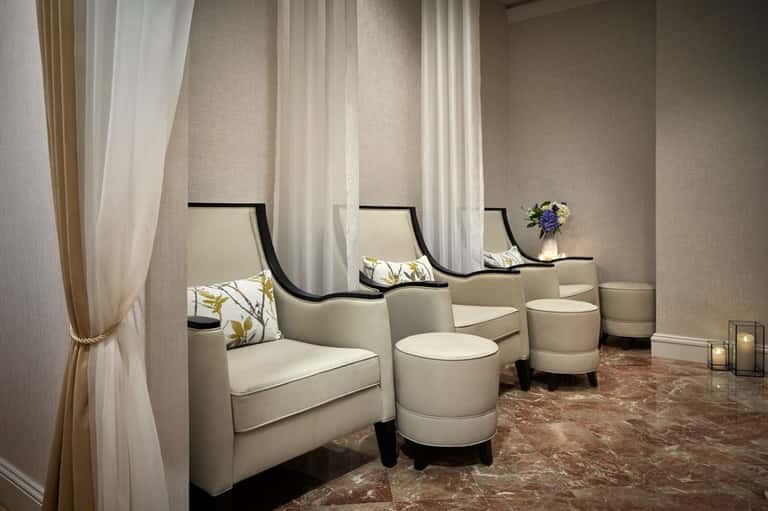 Modern spa waiting area with cream-colored armchairs, floor-to-ceiling curtains, and subtle lighting