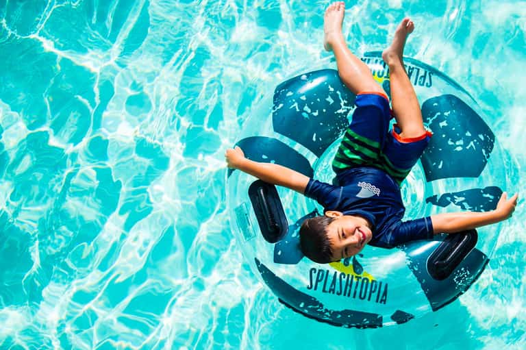 Child floating on inflatable raft in bright turquoise swimming pool with water ripples visible