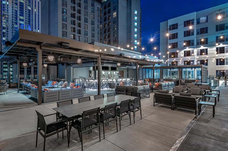 Modern rooftop terrace at dusk with dining tables, lounge seating, and city skyline