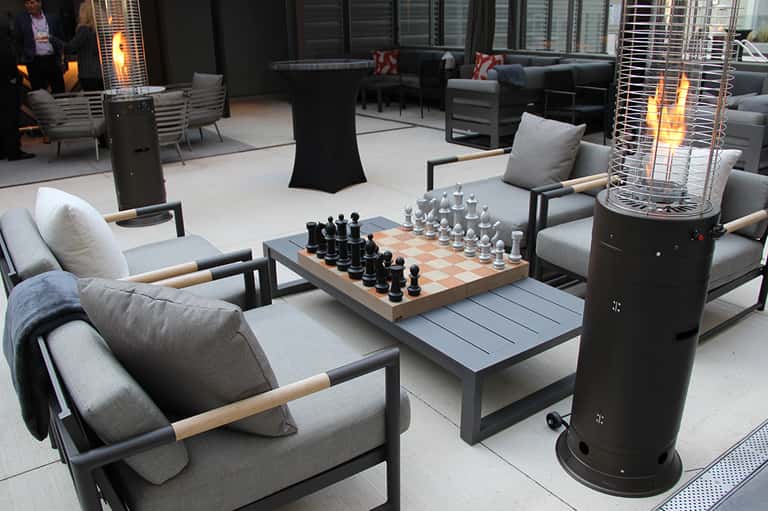 Elegant rooftop lounge with comfortable seating, chess set, heaters, and city views at dusk