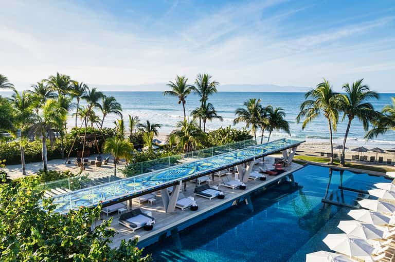 Oceanfront infinity pool with white loungers overlooking beach and palm trees