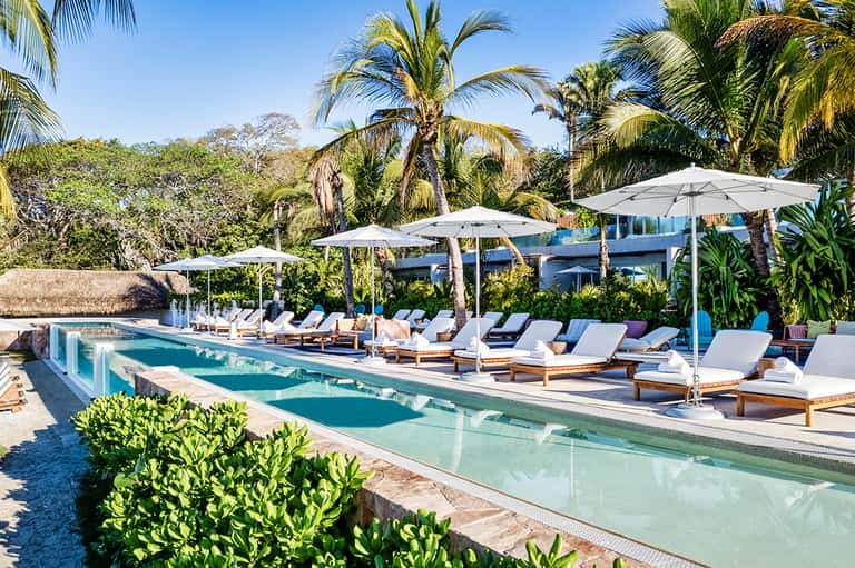 Infinity pool with white lounge chairs, umbrellas, palm trees, and ocean horizon view