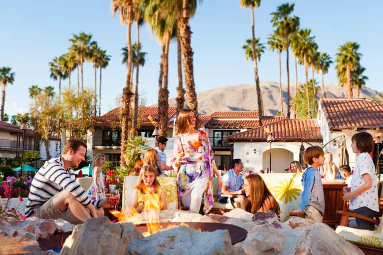 Family gathering around outdoor firepit at resort with Spanish colonial architecture and palm trees