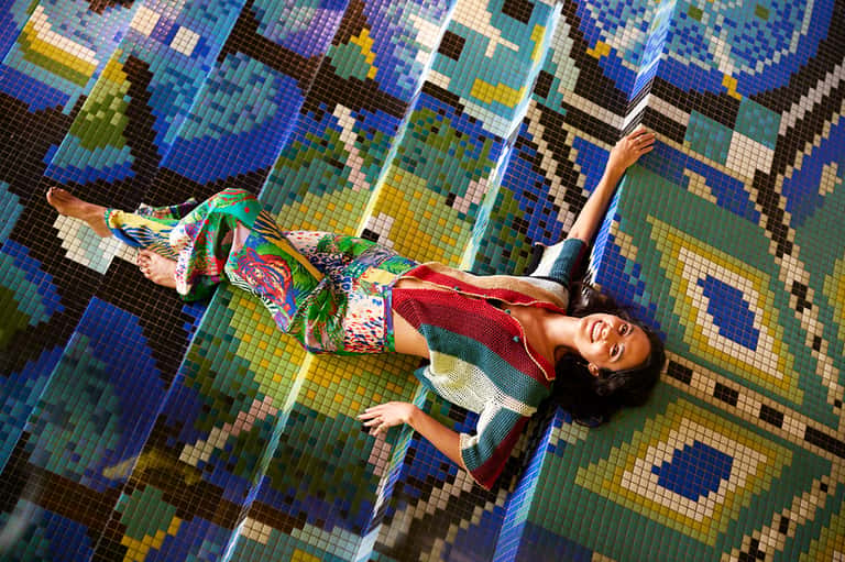 Woman lying on colorful mosaic pool floor in vibrant blue, green, and yellow tiles