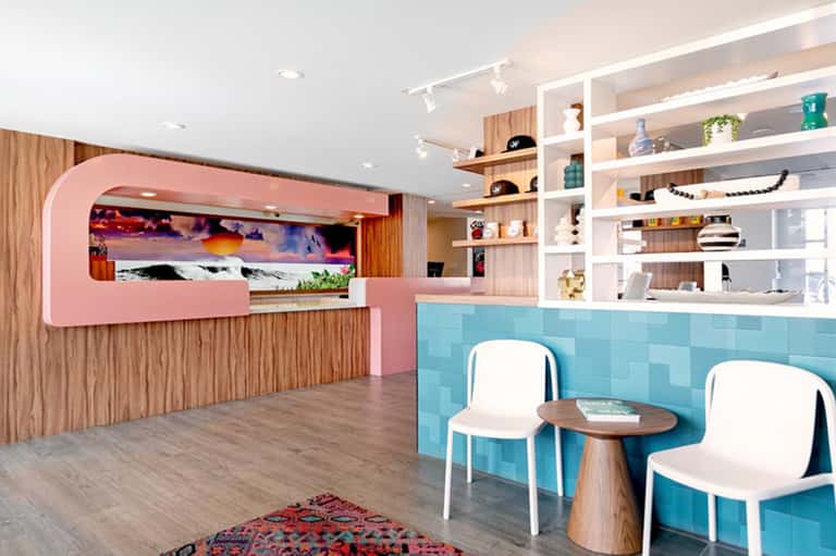 Modern hotel lobby with pink reception desk, turquoise tile accent wall, and white shelving