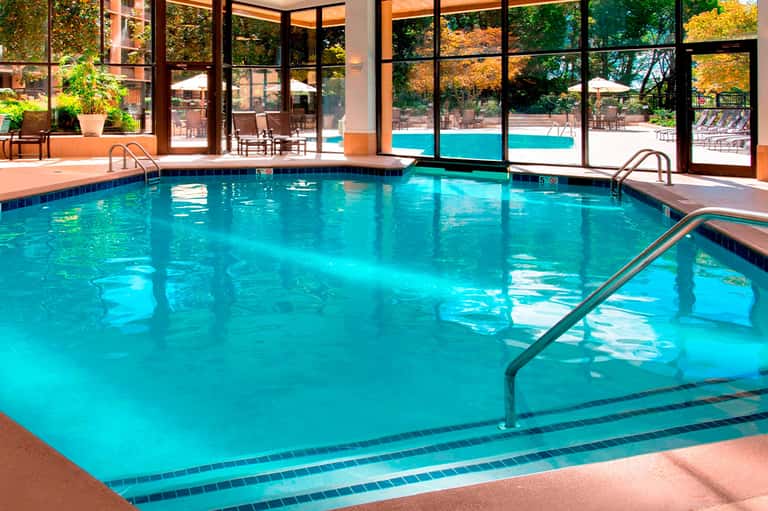 Indoor heated pool with turquoise water, large windows overlooking outdoor pool area