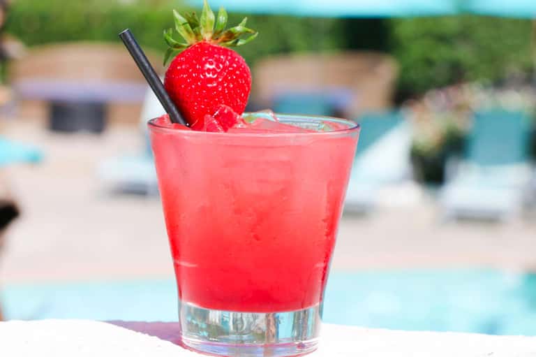 Vibrant red cocktail with fresh strawberry garnish and black straw by poolside