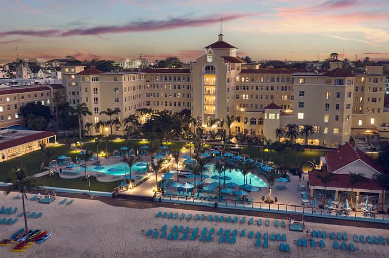 Illuminated resort pools and courtyard at twilight with palm trees and historic-style buildings