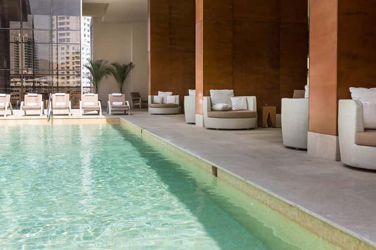 Indoor pool with lounge chairs and modern seating pods overlooking city skyline