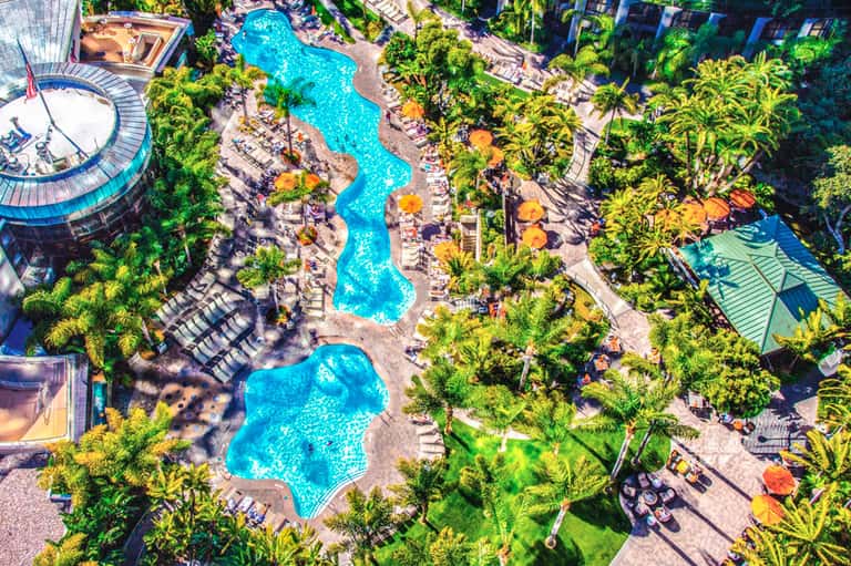 Aerial view of resort with multiple turquoise pools surrounded by palm trees and lounge chairs