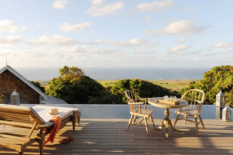 Wooden lounge chairs on deck overlooking ocean, trees, and coastal landscape