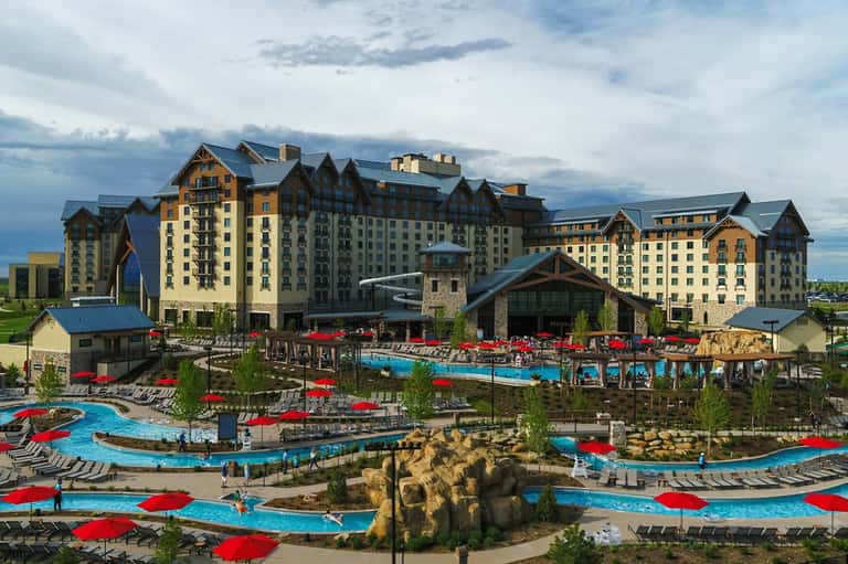 Large lodge-style resort with multiple pools, red umbrellas, water features, and mountain backdrop