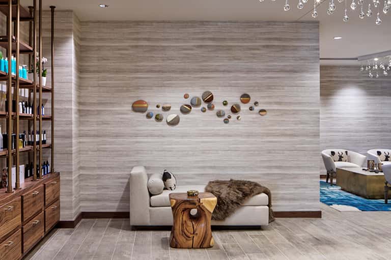 Spa lounge with beige seating, decorative circular mirrors, wood accents, and crystal chandelier