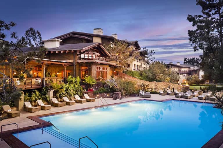 Luxury resort pool at dusk with lodge-style building, loungers, and illuminated landscape