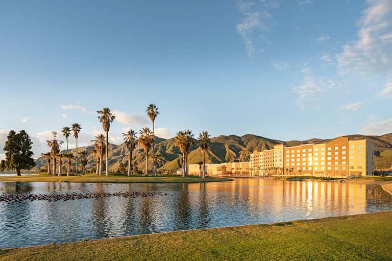 Yellow hotel building reflected in lagoon with palm trees and mountains at sunset