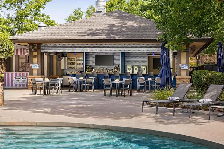 Outdoor pool cabana with bar, dining area, lounge chairs, and shaded pavilion in residential setting